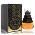 Al Wataniah Oudh Al Aswad unisex EDP, 3.4 fl.oz. Features a striking black and gold bottle with amber liquid, displayed next to its ornate matching box.