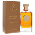 Elegant Azha Woody Drop EDP, clear glass bottle with rich golden fragrance and textured gold cap, beside its matching bronze box.