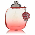 Elegant Coach Floral Blush perfume bottle, clear to vibrant coral gradient glass, with a sleek silver cap and charming red floral accent.