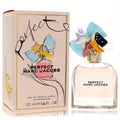 Marc Jacobs Perfect 1.6 oz EDP. Clear bottle with light pink liquid, topped by a whimsical cap adorned with colorful charms like a bow, star, and banana. Matching pink box.