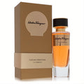 Elegant Salvatore Ferragamo La Commedia 3.3 oz unisex EDP, vibrant orange liquid in a clear glass bottle with gold accents and a matching brown luxury box.